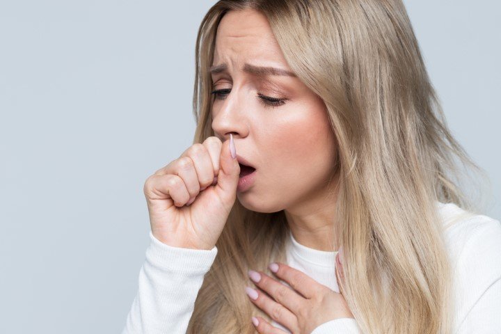 A woman coughing into her fist while holding her chest, appearing uncomfortable and in distress trying to How to Stop Cough at Night 