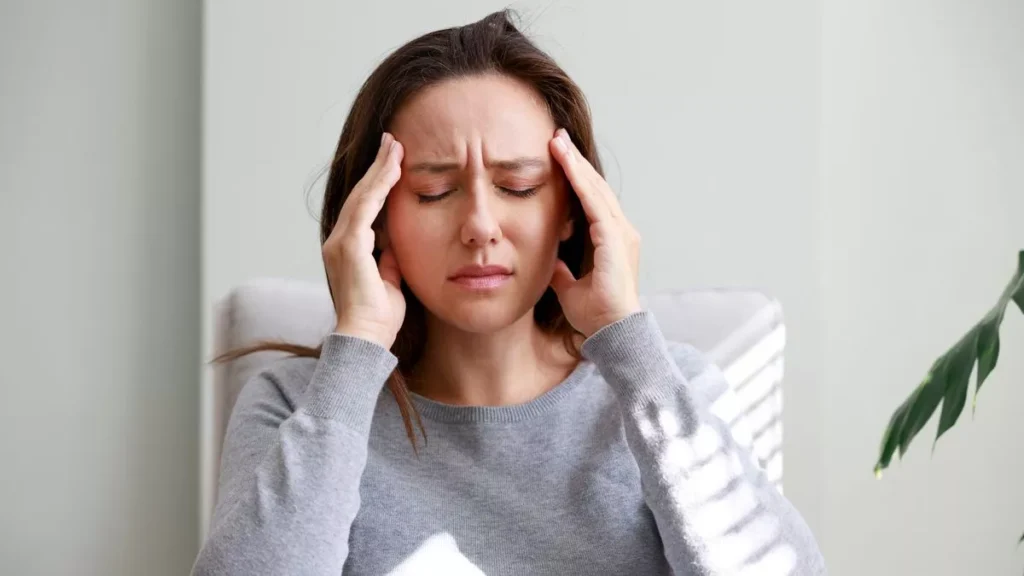 Young woman holding her head in discomfort due to pain at home